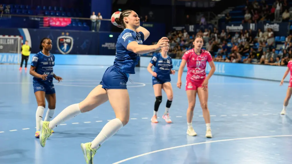 Une joueuse de handball en plein saut s'apprête à tirer au but en match.