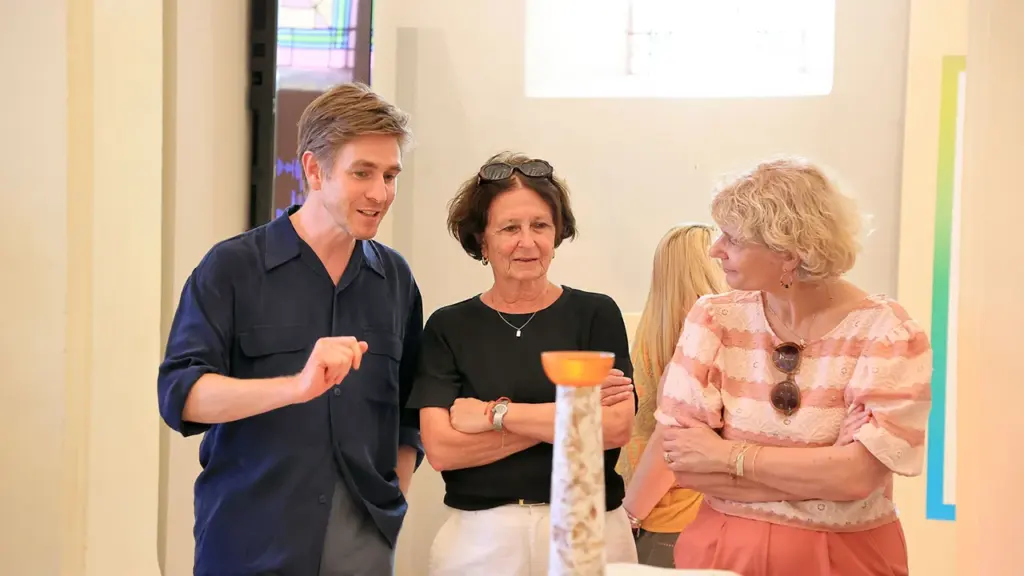Un homme et deux femmes observent attentivement un vase décoratif dans une galerie d'art.