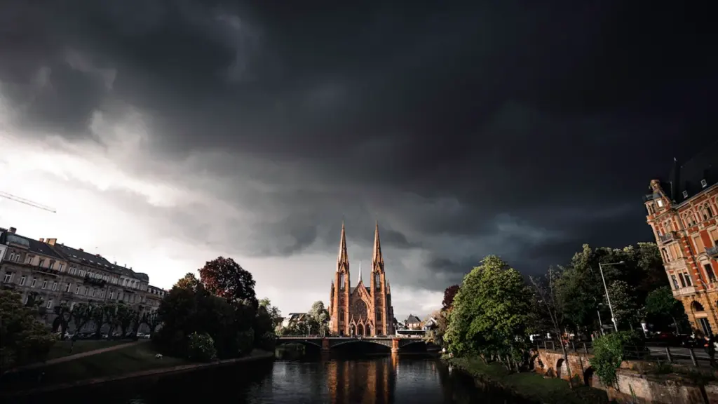 Ciel orageux menaçant au-dessus d'une église et d'une rivière calme.