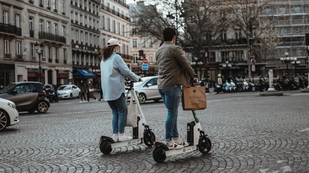 Deux personnes utilisant des trottinettes électriques sur une place pavée à Paris.
