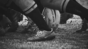 Gros plan en noir et blanc sur un ballon de rugby au sol.