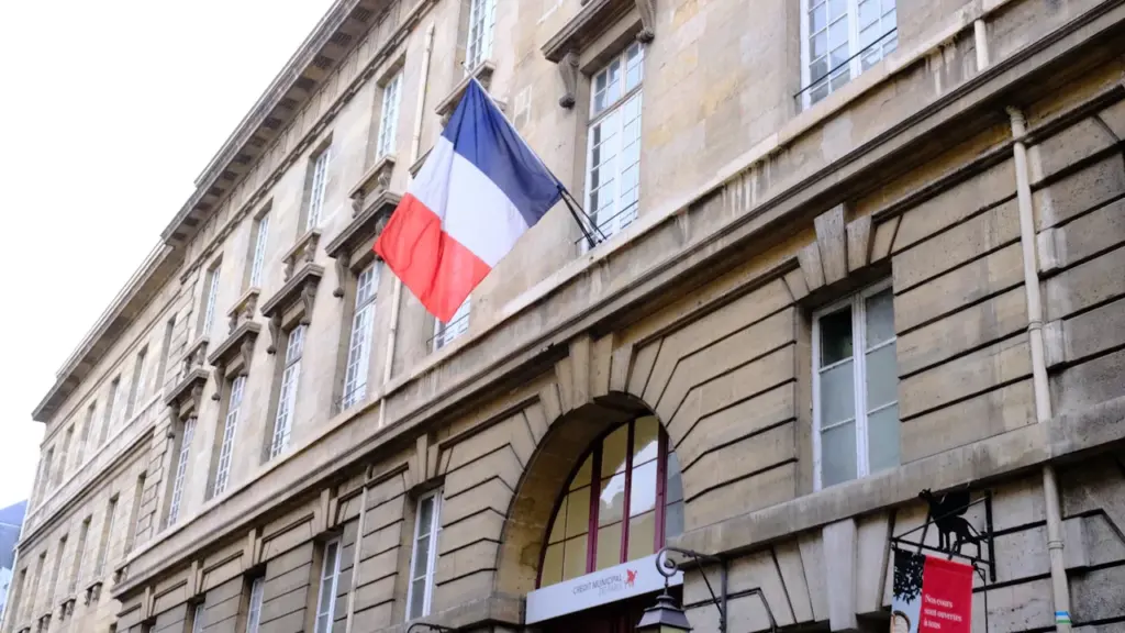 Un drapeau français flotte sur un bâtiment en pierre institutionnel classique à Paris.