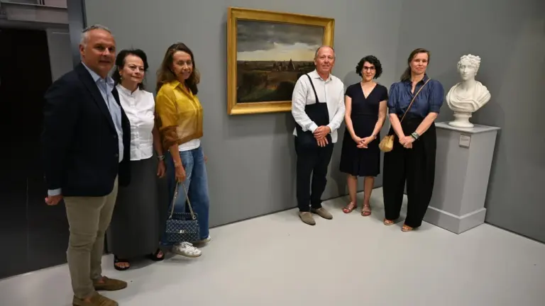 Un groupe de six personnes pose devant un tableau ancien et un buste sculpté.