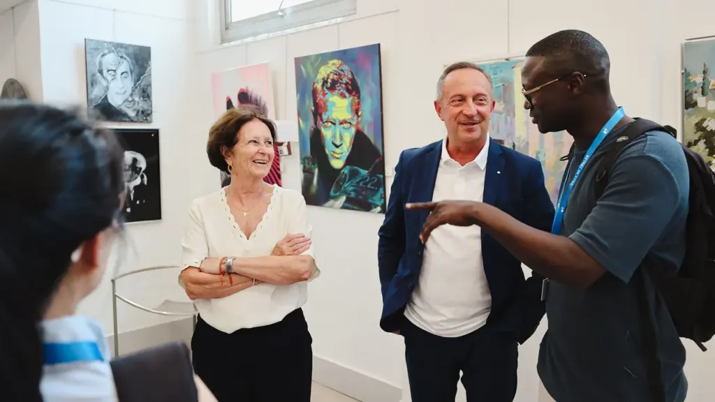 Trois personnes discutent joyeusement dans une galerie d'art devant des peintures contemporaines colorées.