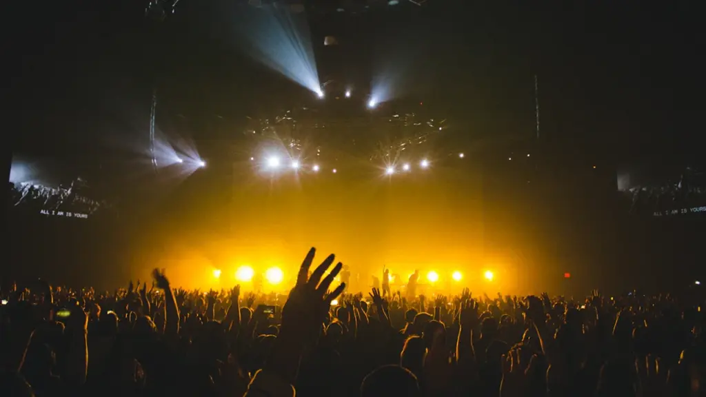 Foule enthousiaste assistant à un concert sous des projecteurs jaunes éclatants.