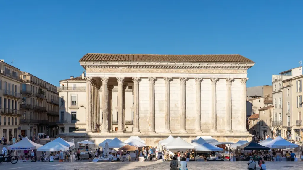 Le temple romain antique Maison Carrée à Nîmes entouré de tentes de marché sous ciel bleu.