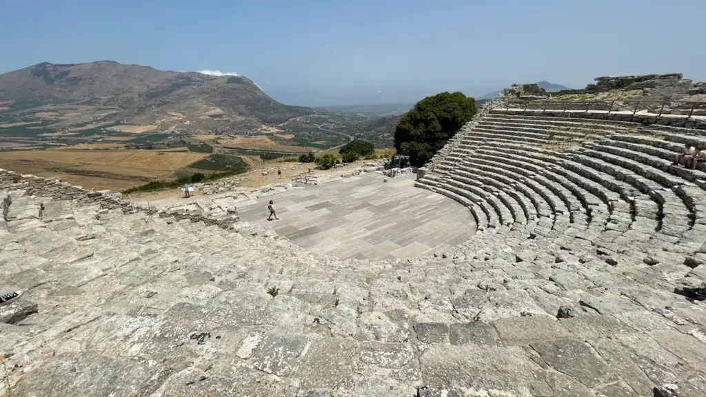 Vue panoramique d'un amphithéâtre antique en pierre surplombant un paysage vallonné en été.