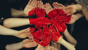Plusieurs mains peintes en rouge formées ensemble en forme de cœur solidaire.