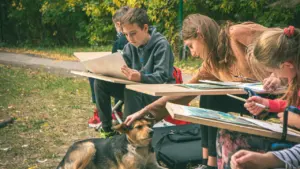 Des enfants dessinant en plein air avec un chien dans un parc public.