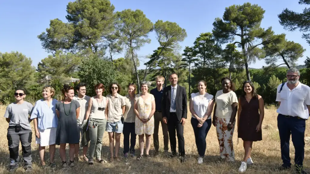 Un groupe diversifié de personnes pose devant une forêt sous un ciel bleu dégagé.