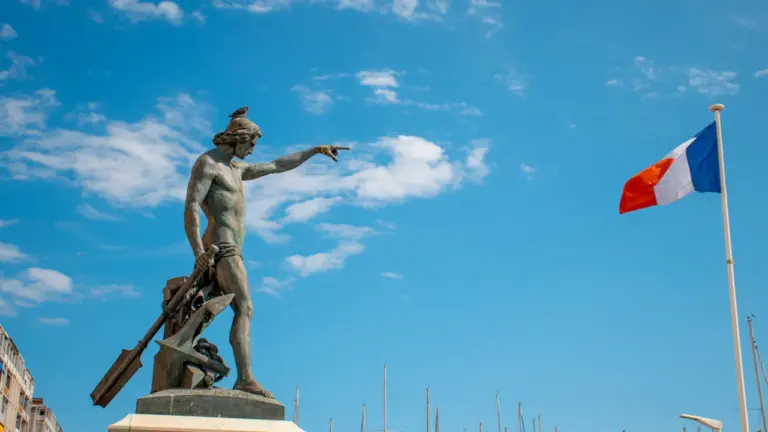 Statue de marin devant le drapeau français dans le port de Toulon.
