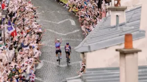 Deux cyclistes roulent sur une route pavée entourée d'une foule enthousiaste lors d'une course.