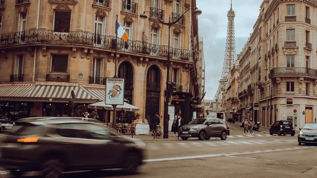 Vue urbaine parisienne avec circulation automobile près d'un café et la Tour Eiffel.