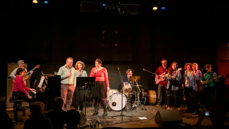 Un groupe de musiciens amateurs joue de la musique sur une scène sombre éclairée.