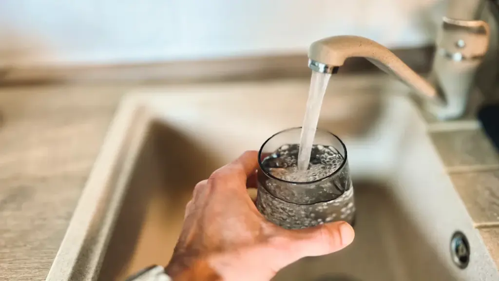 Une main tenant un verre d'eau sous un robinet dans une cuisine moderne.