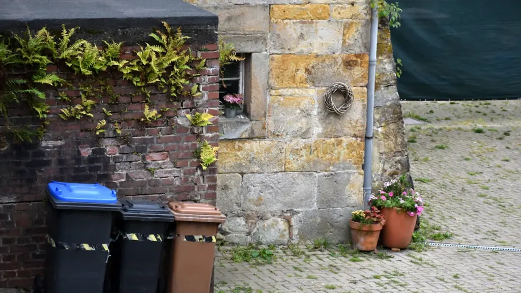Poubelles ménagères devant un mur en pierre typique d'une maison bretonne traditionnelle.
