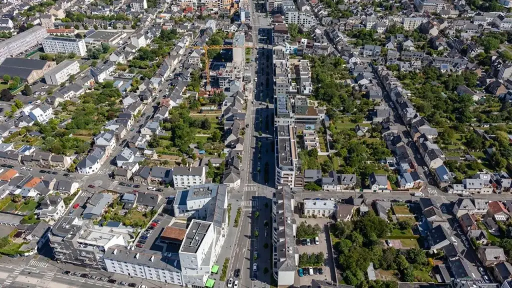 Vue aérienne d'une ville dense avec une longue avenue entourée de maisons et jardins.