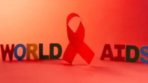 Un ruban rouge symbolique placé devant le texte coloré WORLD AIDS sur fond rouge.
