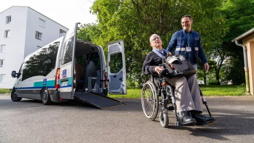 Un homme en fauteuil roulant assisté par un accompagnateur près d'un véhicule adapté accessible.